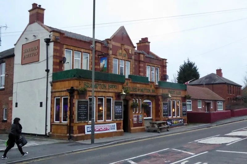 The Shoulder of Mutton pub in Hasland, a red-brick and glazed orange tile building with a gabled front and a hanging sign, beside the road, with one pedestrian walking past.